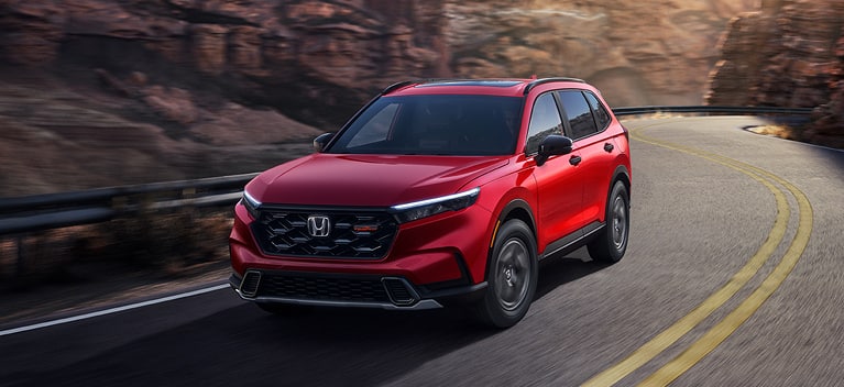 2027 Honda CR-V TrailSport Hybrid in Radiant Red Metallic front driving on a winding mountain road (Compact Crossover SUV).